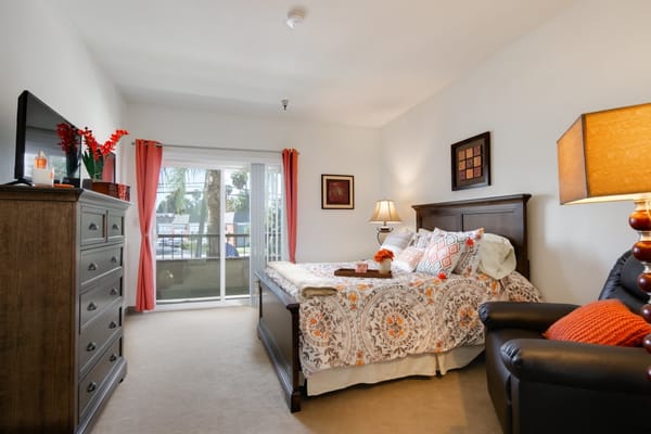 Cozy bedroom featuring a bed, dresser, and balcony view with palm trees.