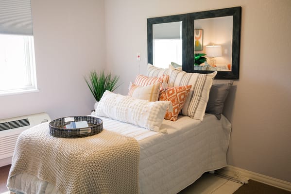 A well-decorated bedroom with colorful pillows and a view of a window.