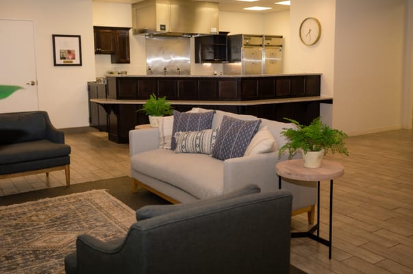 Lounge seating area with a gray sofa and chairs, decorated with plants.