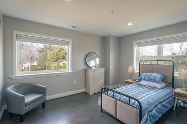 A neatly arranged bedroom with a bed, dresser, and seating area.