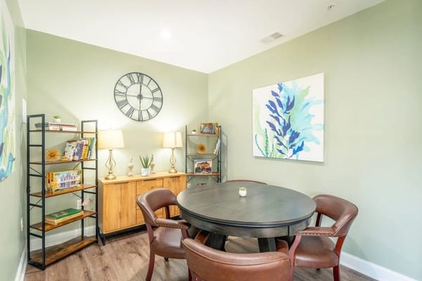 A common area with a round table, chairs, and a bookshelf