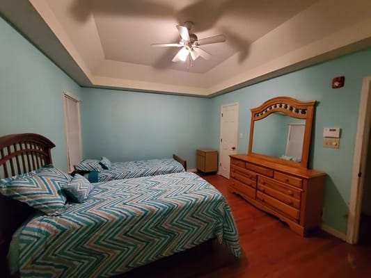 A cozy bedroom with two beds, a dresser, and a ceiling fan.