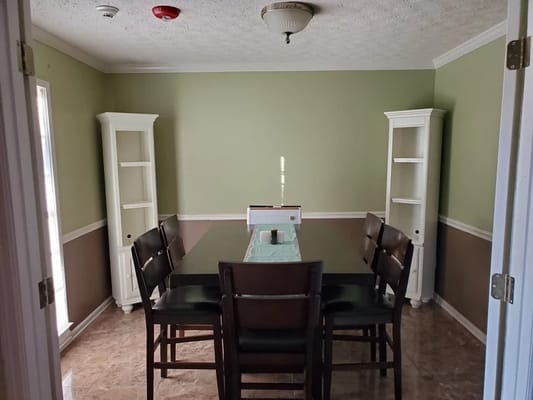 A dining room with a long table and chairs in a warm green setting.