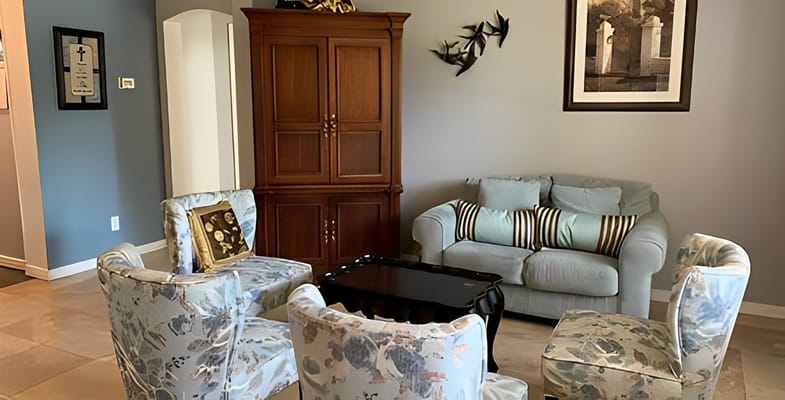 A cozy living room with a blue sofa, floral chairs, and wooden cabinet.