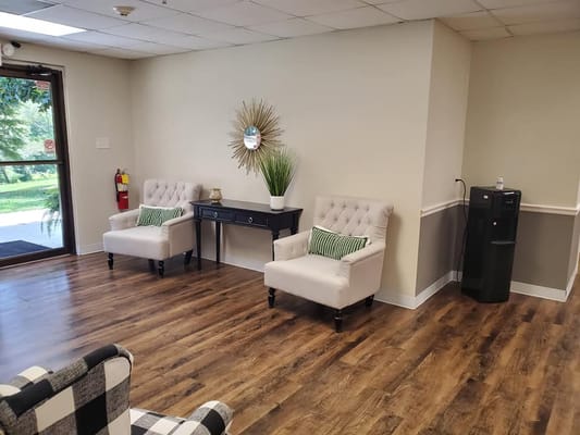 A bright lounge area featuring two armchairs, a table, and greenery decor.