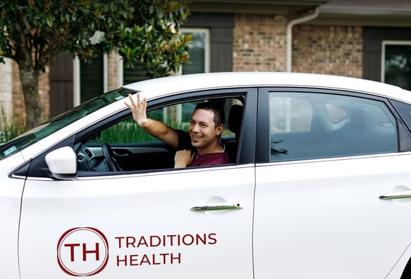 A smiling driver waves from a Traditions Health vehicle.