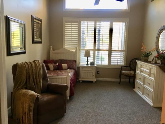 A cozy bedroom with a bed, armchair, and dresser, featuring plantation shutters.