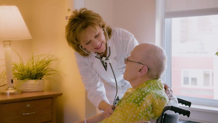 A healthcare professional interacts with a resident in a warm, inviting room.