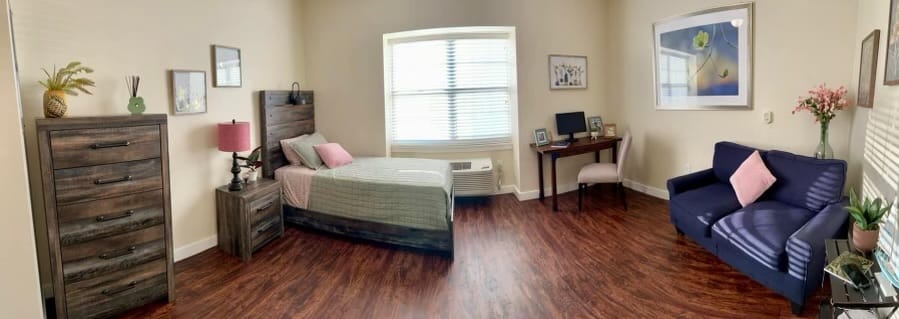 A cozy bedroom featuring a bed, dresser, and seating area.