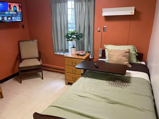 Interior view of a private room with a bed, chair, and TV.