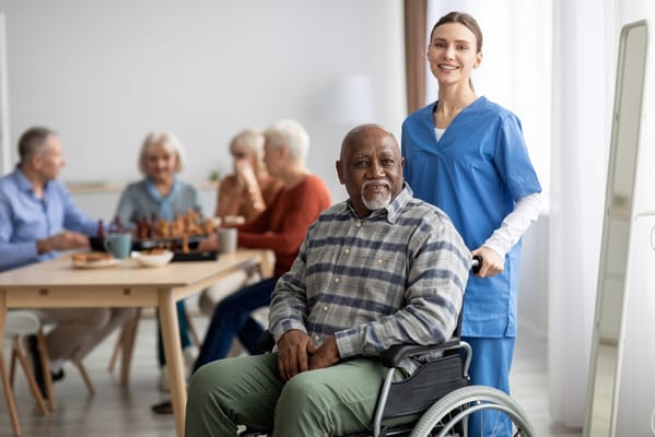 A caregiver assisting a resident in a wheelchair in a communal game area.