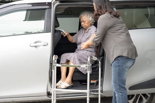 Caregiver assisting an elderly woman into a vehicle