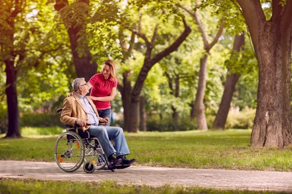 A caregiver assisting a resident in a park setting.