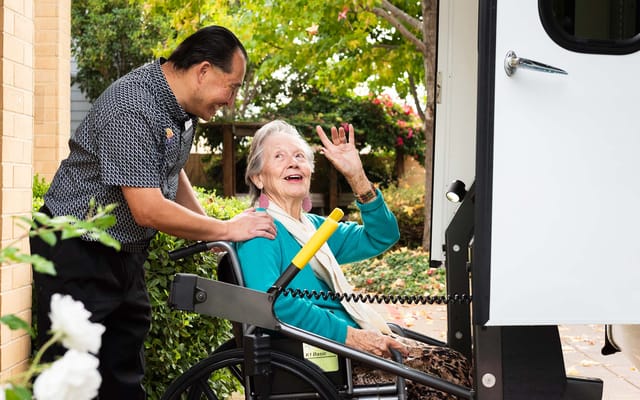 Resident joyfully interacting with staff by a facility vehicle