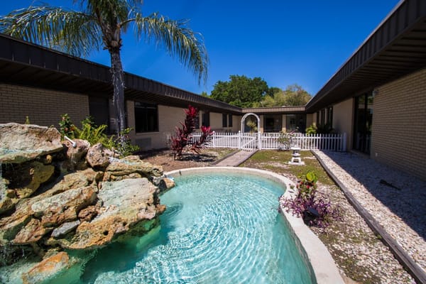 A serene courtyard with a pool, stone features, and tropical plants