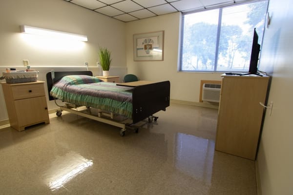 Private bedroom with a bed, nightstand, and television in a senior living facility.