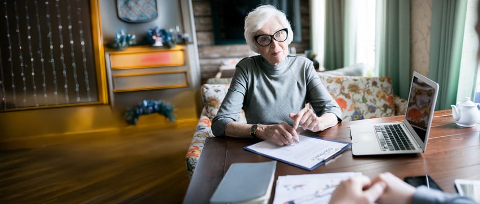 An elderly woman talking at a table with a laptop