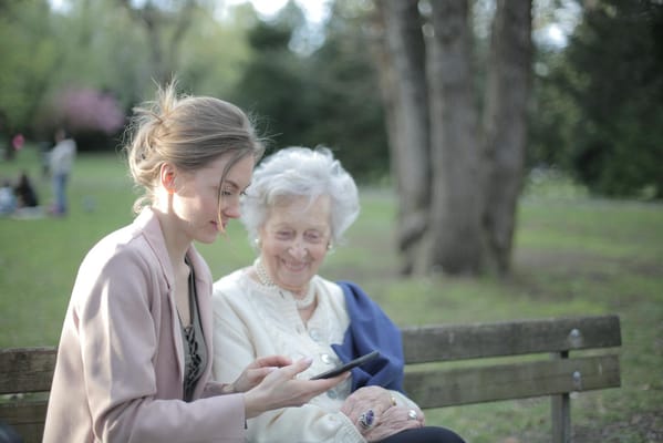 A young woman showing a tablet to an elderly woman in a park