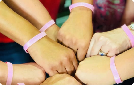 Several hands wearing pink wristbands coming together