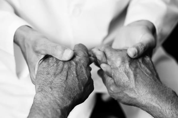 Close-up of hands clasped between caregiver and resident