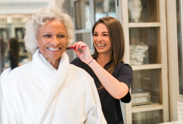 A caregiver styling a resident's hair in a bright room