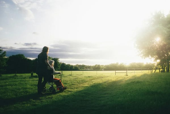 A caregiver walking with a senior in a grassy outdoor area