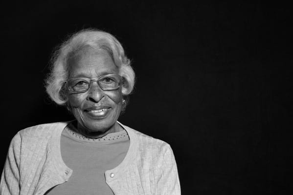 An elderly woman smiling against a dark background