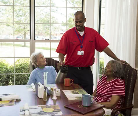 Staff serving tea to elderly residents in a bright common area