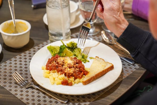 A resident enjoying a meal with pasta and broccoli.