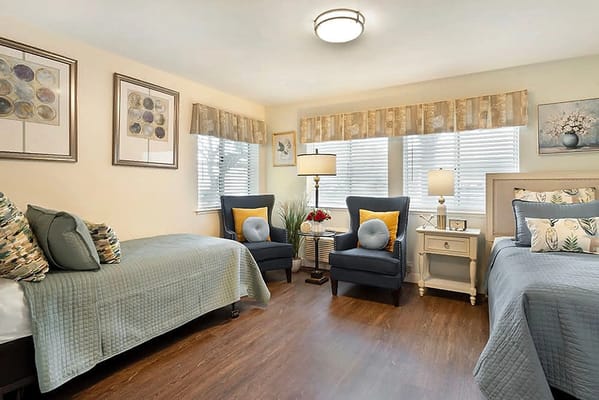 A well-decorated bedroom with two beds, comfortable chairs, and natural light.