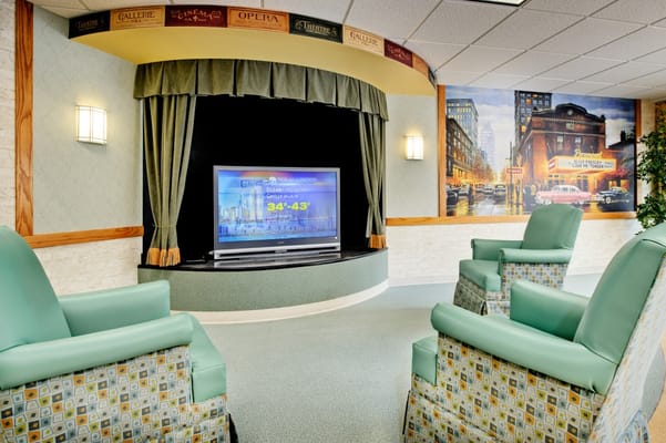 Lounge area with two green chairs and a TV in a healthcare facility