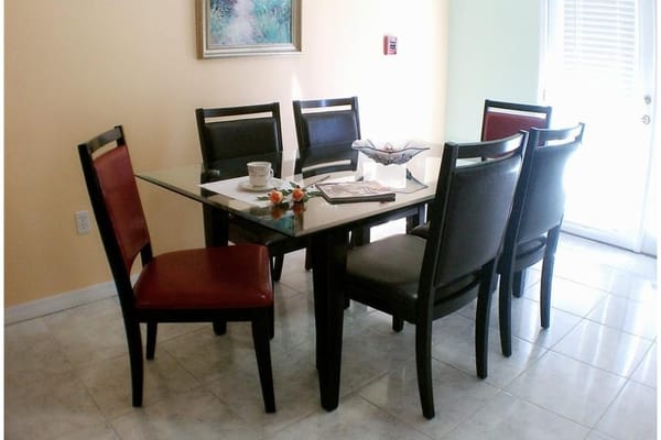 A glass dining table surrounded by six chairs in a bright room.