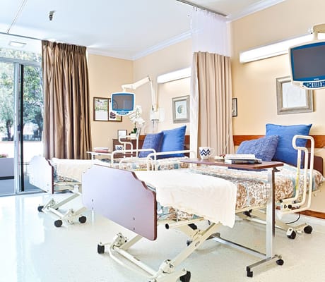 Two hospital beds in a bright patient room with a large window.