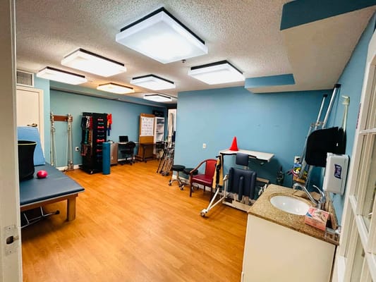 A spacious therapy room with exercise equipment and wooden flooring.