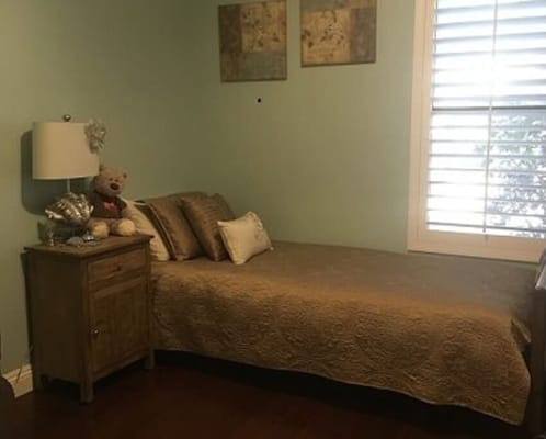 A cozy bedroom with a single bed, lamp, and teddy bear.