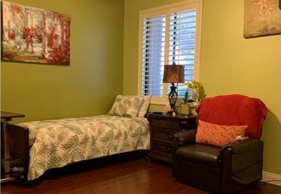 A cozy bedroom with a single bed, armchair, and decorative art on green walls.