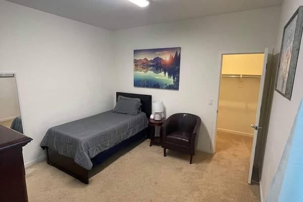 A simple bedroom with a bed, nightstand, and armchair.