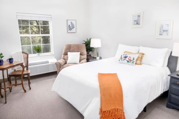 A comfortable bedroom with a bed, armchair, and window.