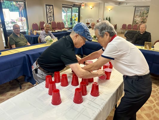 Two seniors competing in a cup stacking game at a dining area.