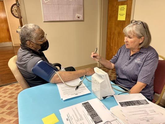 A staff member checks a resident's blood pressure at a table.