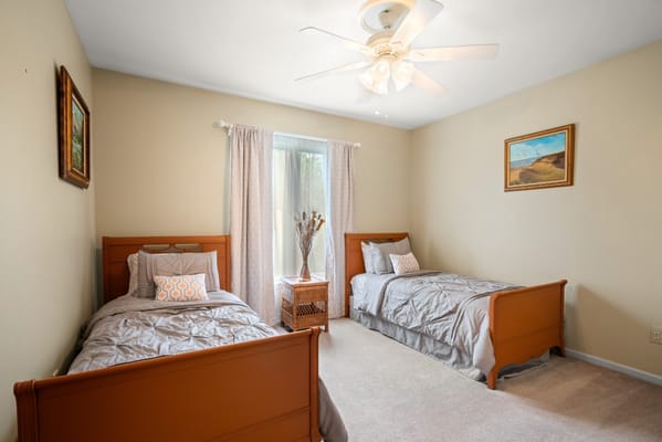 A cozy bedroom with two twin beds, a window, and a decorative table.