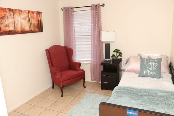 A well-decorated bedroom with a red armchair and a bed adorned with a 'Happy Place' pillow.