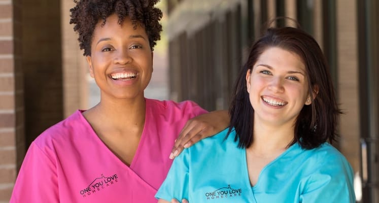 Two smiling caregivers in scrubs at One You Love Homecare