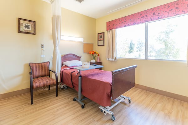 A neatly arranged bedroom in a senior living facility featuring a hospital bed and a striped chair.