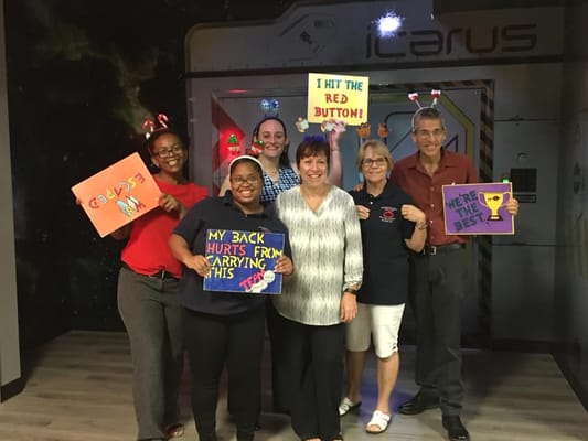 Staff members holding signs and smiling in a themed room.