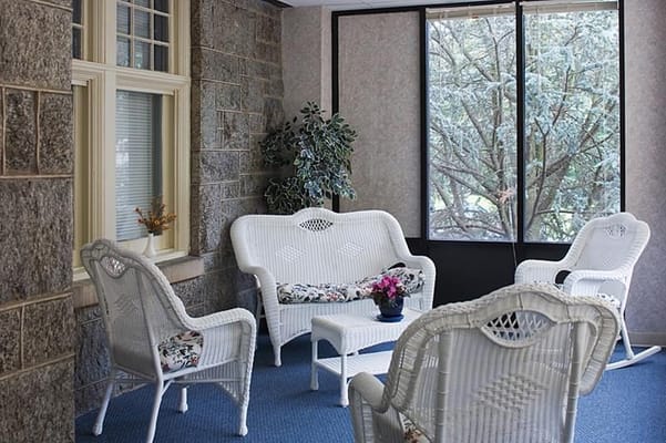 A cozy sunroom with white wicker furniture and potted plants.