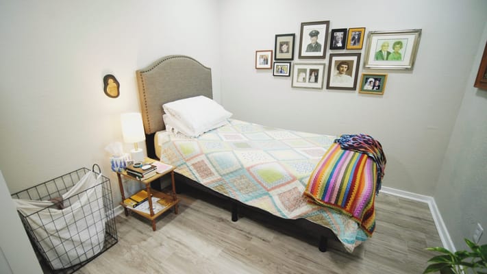A cozy bedroom featuring a bed, colorful quilt, and family photos on the wall.