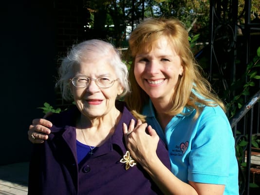 A caregiver and a senior resident smiling together outdoors.