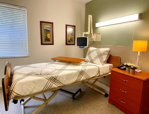 A private room with a hospital bed, bedside table, and artwork