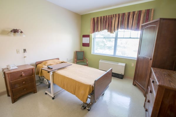 An inviting bedroom with a hospital bed, chair, and wooden furniture.